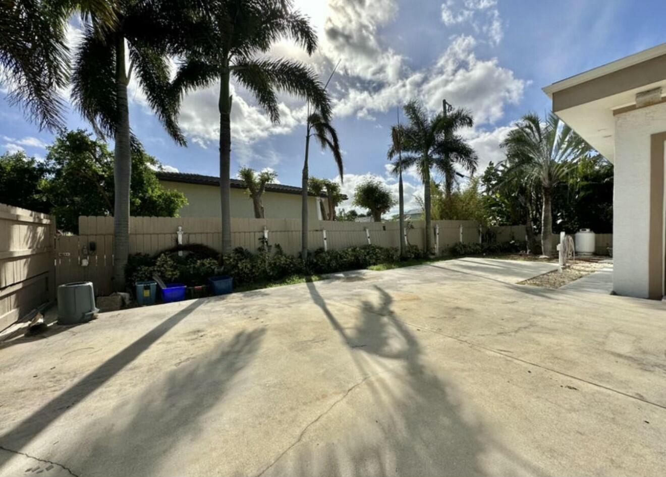A concrete patio area features palm trees, a wooden fence, and a white house exterior — 698 Forsyth Street # 2, Boca Raton FL 33487, BOCA RATON, FL