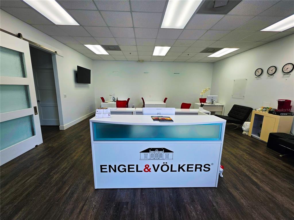 A modern office reception area features a branded white desk, wood flooring, and drop ceiling — 7600 DR. PHILLIPS BOULEVARD UNIT 53, ORLANDO, FL
