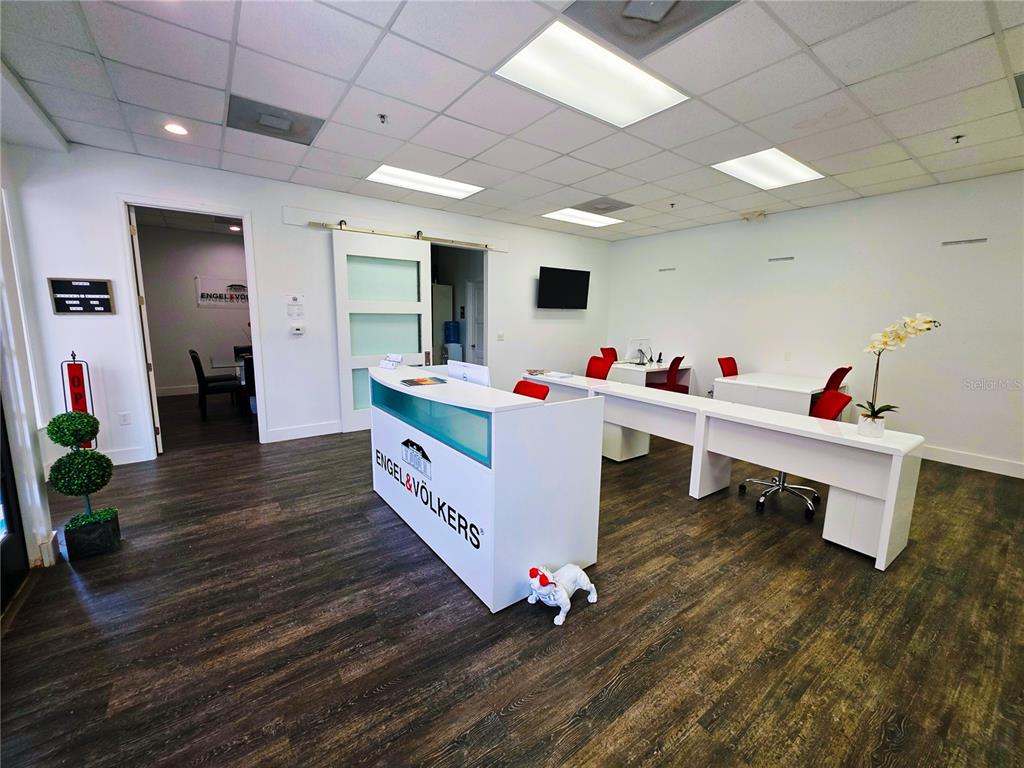 A modern office space features a reception desk, white workstations, and dark wood-look flooring — 7600 DR. PHILLIPS BOULEVARD UNIT 53, ORLANDO, FL