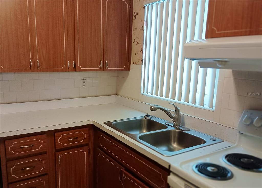 A kitchen features wood cabinets, a double-basin stainless steel sink, and white countertops — 1875 SUNNY DRIVE UNIT G32, BRADENTON, FL