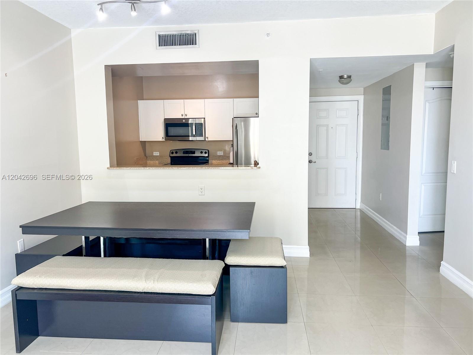 A dining area with a dark table and benches sits before a kitchen pass-through window — 117 NW 42nd Ave # 506, Miami FL 33126, MIAMI, FL