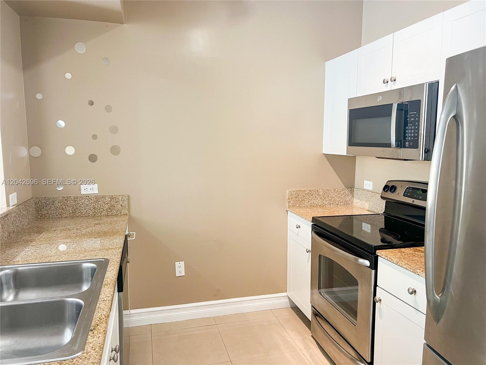 A kitchen features stainless steel appliances, white cabinetry, and tan granite countertops — 117 NW 42nd Ave # 506, Miami FL 33126, MIAMI, FL
