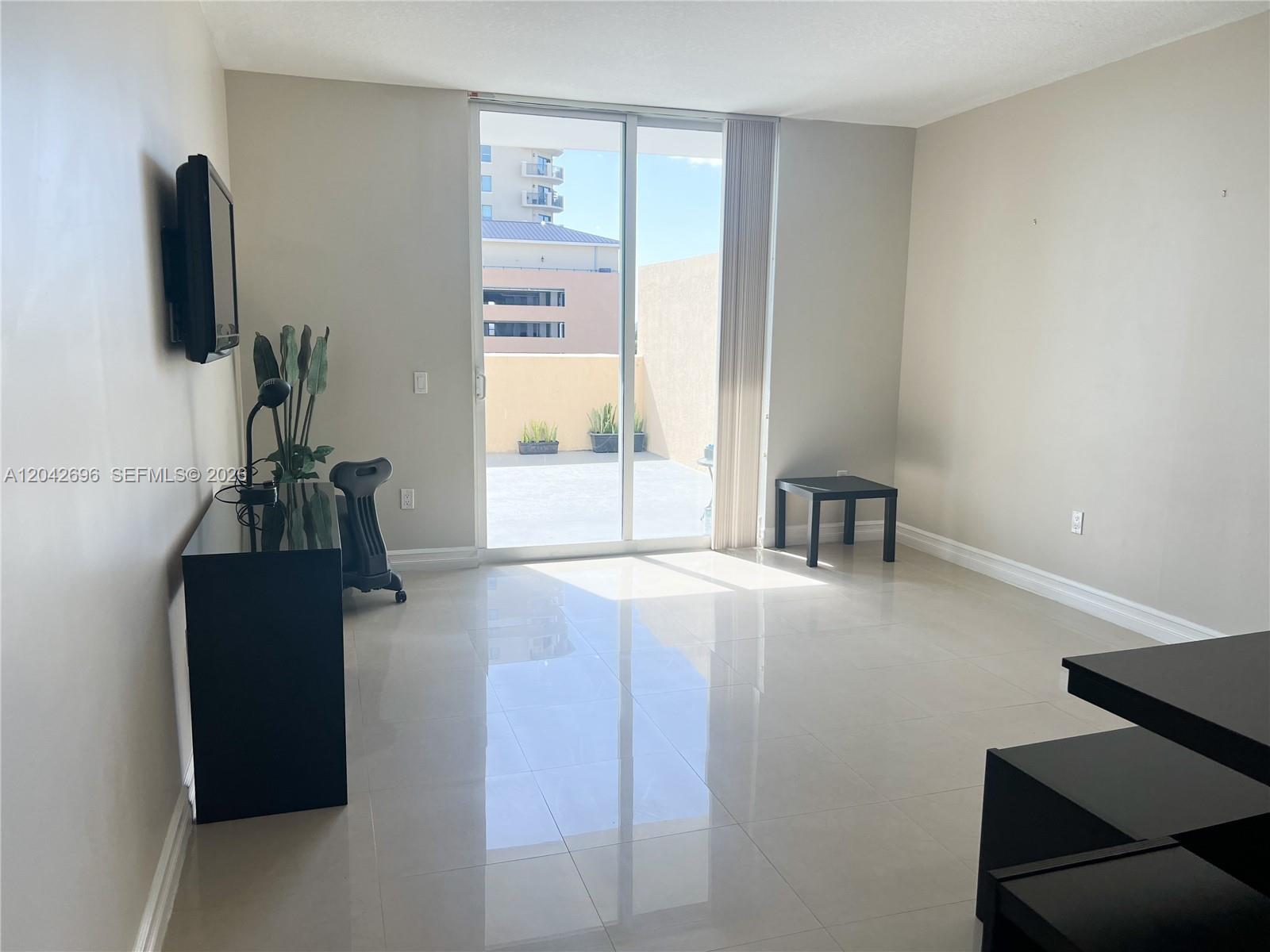 A bright living room features light tile floors, a sliding glass door, and a balcony — 117 NW 42nd Ave # 506, Miami FL 33126, MIAMI, FL