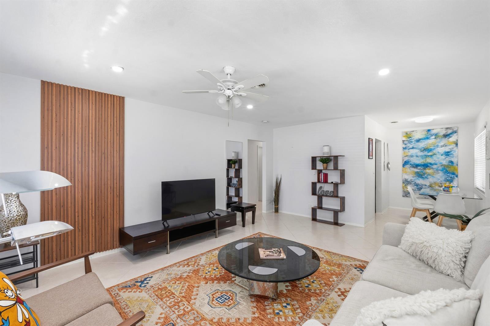 A living room features a wood-slat accent wall, a circular glass coffee table, and tile flooring — 23 NE 19th Avenue, Pompano Beach FL 33060, POMPANO BEACH, FL