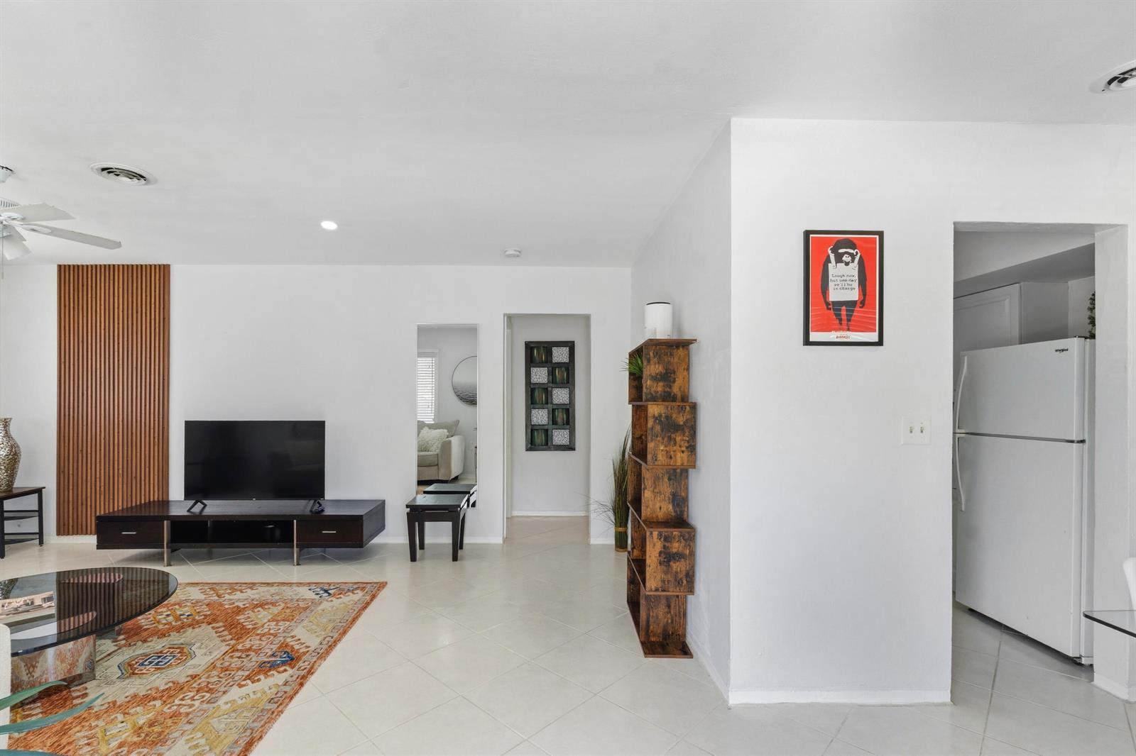 A living room features white walls, tile flooring, a wood-slat accent wall, and a bookshelf — 23 NE 19th Avenue, Pompano Beach FL 33060, POMPANO BEACH, FL