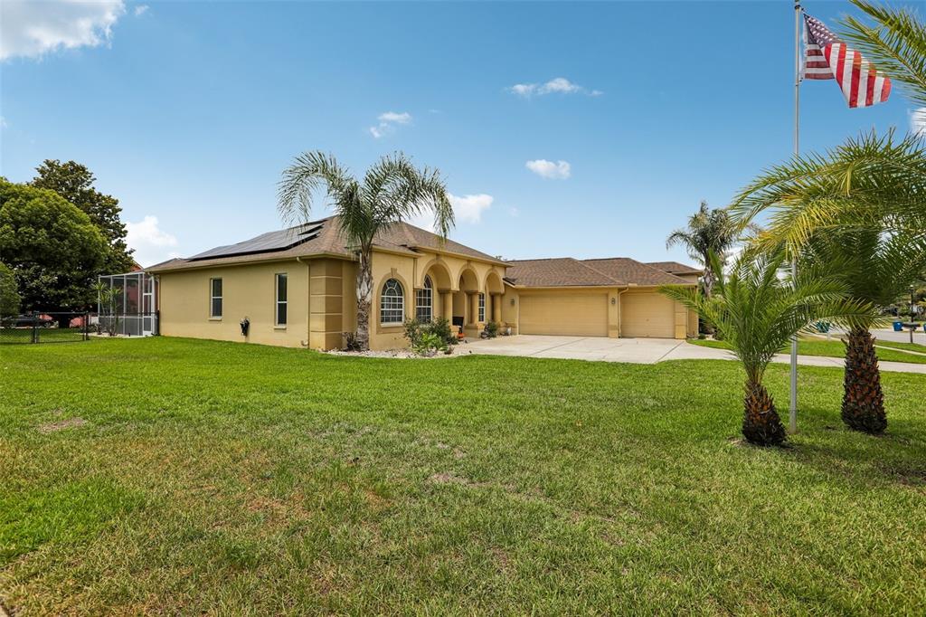 A tan single-story house with a three-car garage, solar panels, and palm trees — 3542 CONIFER LOOP, SPRING HILL, FL
