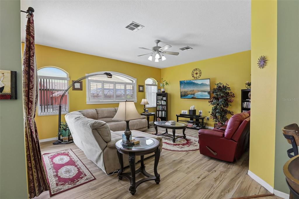 A living room with yellow walls, wood-look flooring, a sectional sofa, and a red recliner — 3542 CONIFER LOOP, SPRING HILL, FL