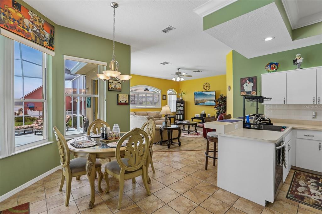 An open-concept kitchen and dining area features tile flooring, green and yellow walls, and furniture — 3542 CONIFER LOOP, SPRING HILL, FL