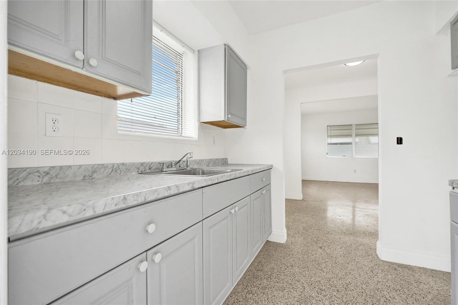 A kitchen features gray cabinets, a marble-patterned countertop, and an adjacent living area — 710 82nd St # 1, Miami Beach FL 33141, MIAMI BEACH, FL