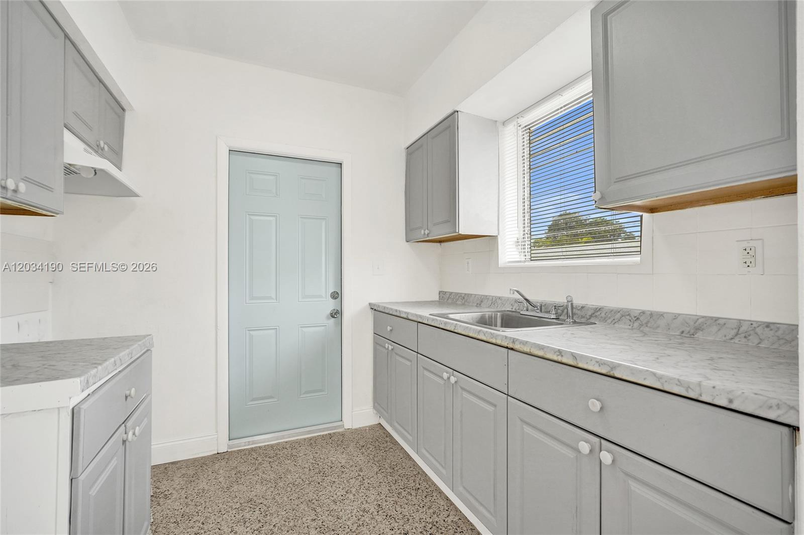A kitchen features gray cabinets, marble-patterned countertops, a stainless steel sink, and a light-blue door — 710 82nd St # 1, Miami Beach FL 33141, MIAMI BEACH, FL