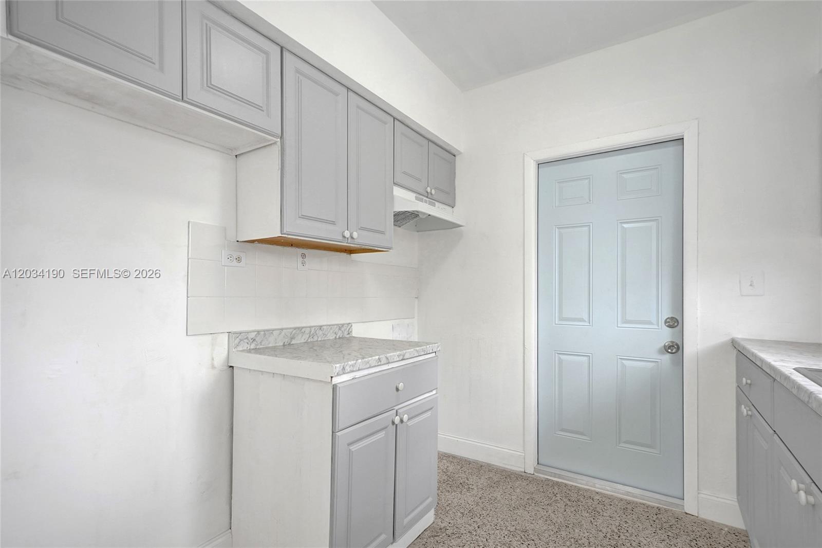 A kitchen features gray cabinets, white walls, a light blue door, and speckled flooring — 710 82nd St # 1, Miami Beach FL 33141, MIAMI BEACH, FL