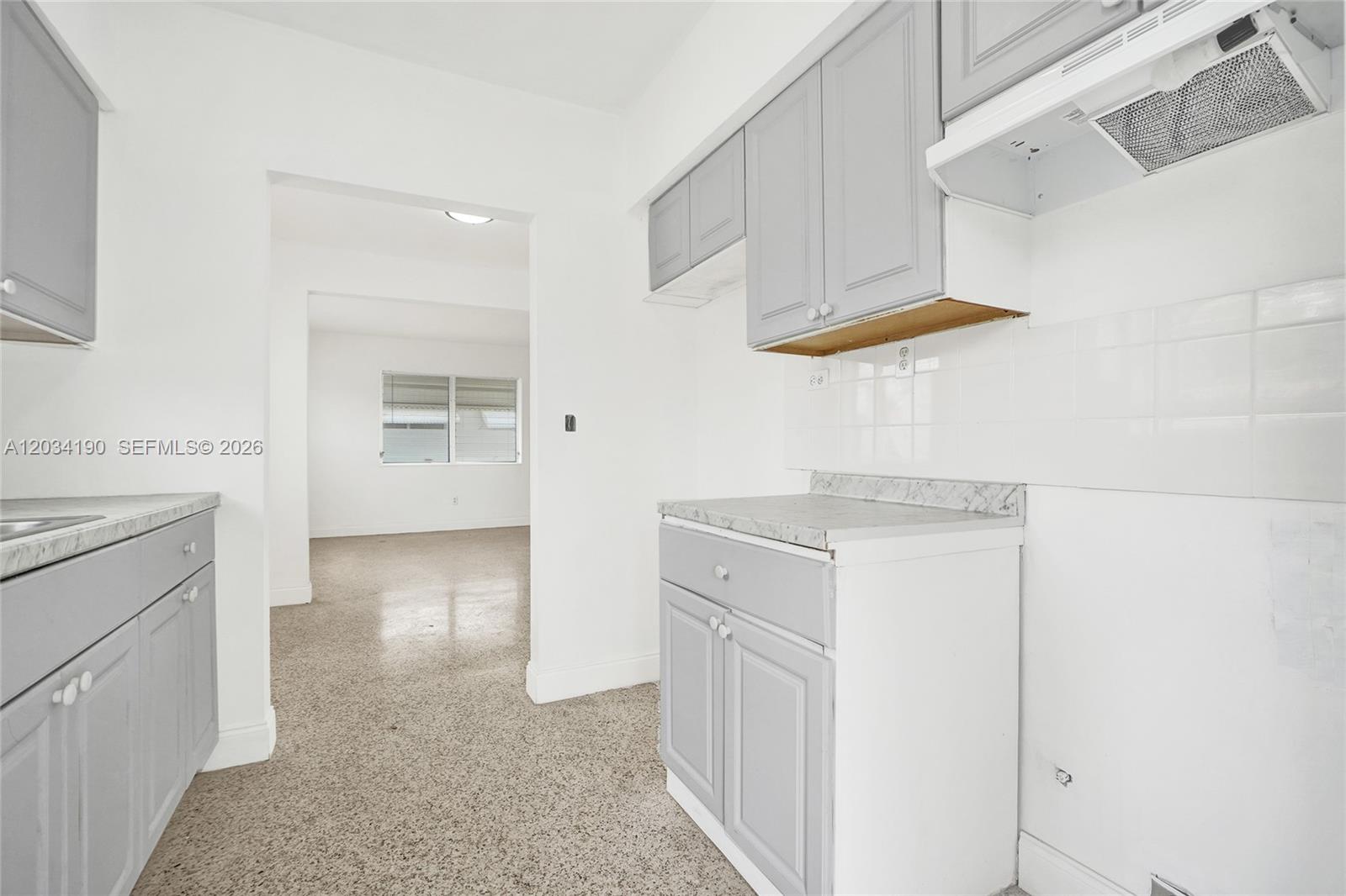 A kitchen features light gray cabinets, white tile backsplashes, and speckled flooring — 710 82nd St # 1, Miami Beach FL 33141, MIAMI BEACH, FL