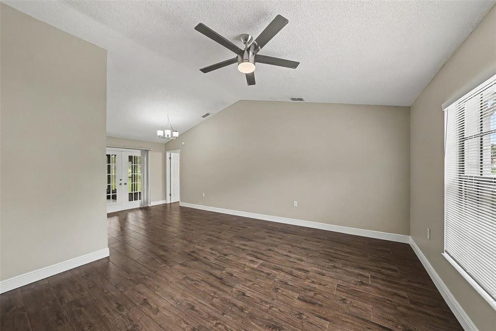 A living room features wood-look tile flooring, a vaulted ceiling with a fan, and glass doors — 8009 PAGODA DRIVE, SPRING HILL, FL