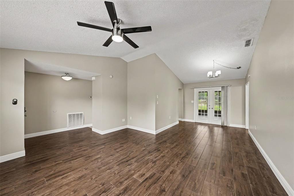 An empty living room features vaulted ceilings, a ceiling fan, and dark wood-look tile flooring — 8009 PAGODA DRIVE, SPRING HILL, FL