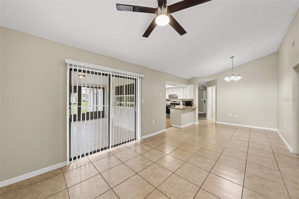 A tiled living area features a ceiling fan, sliding glass doors, and an open kitchen — 8009 PAGODA DRIVE, SPRING HILL, FL