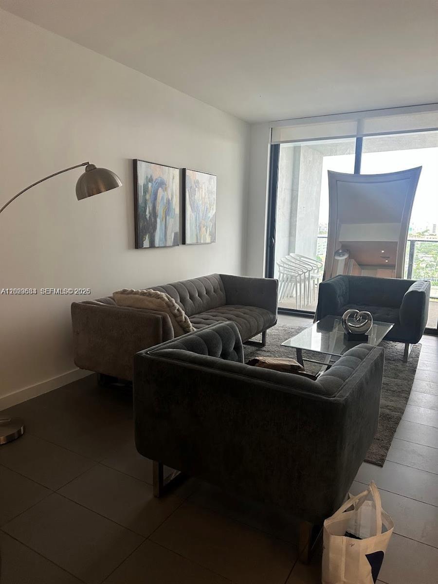 A modern living room features gray tufted furniture, a glass coffee table, and floor-to-ceiling windows — 1600 NE 1st Ave # 1612, Miami FL 33132, MIAMI, FL