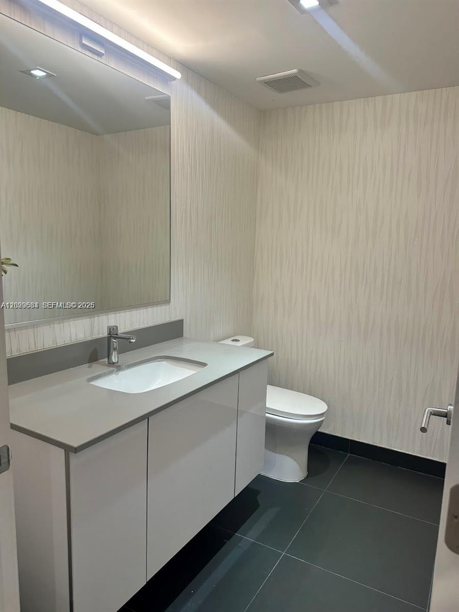 A modern bathroom features a white vanity, gray countertop, large mirror, and dark floor tiles — 1600 NE 1st Ave # 1612, Miami FL 33132, MIAMI, FL