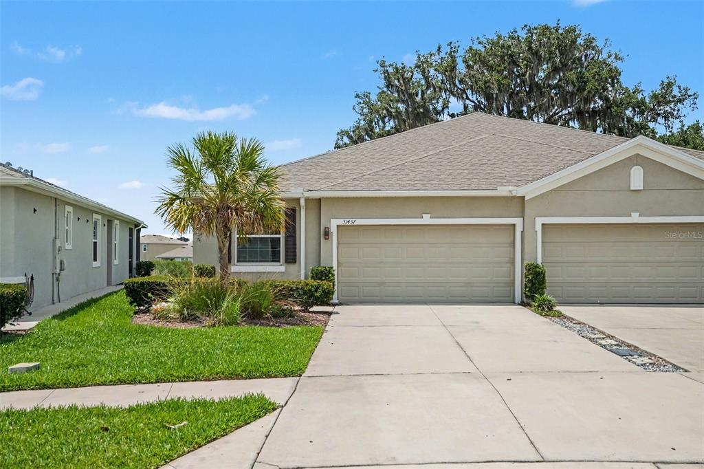 A tan, single-story duplex with a two-car garage and a small palm tree in front — 31457 MANGO FADE WAY, SAN ANTONIO, FL