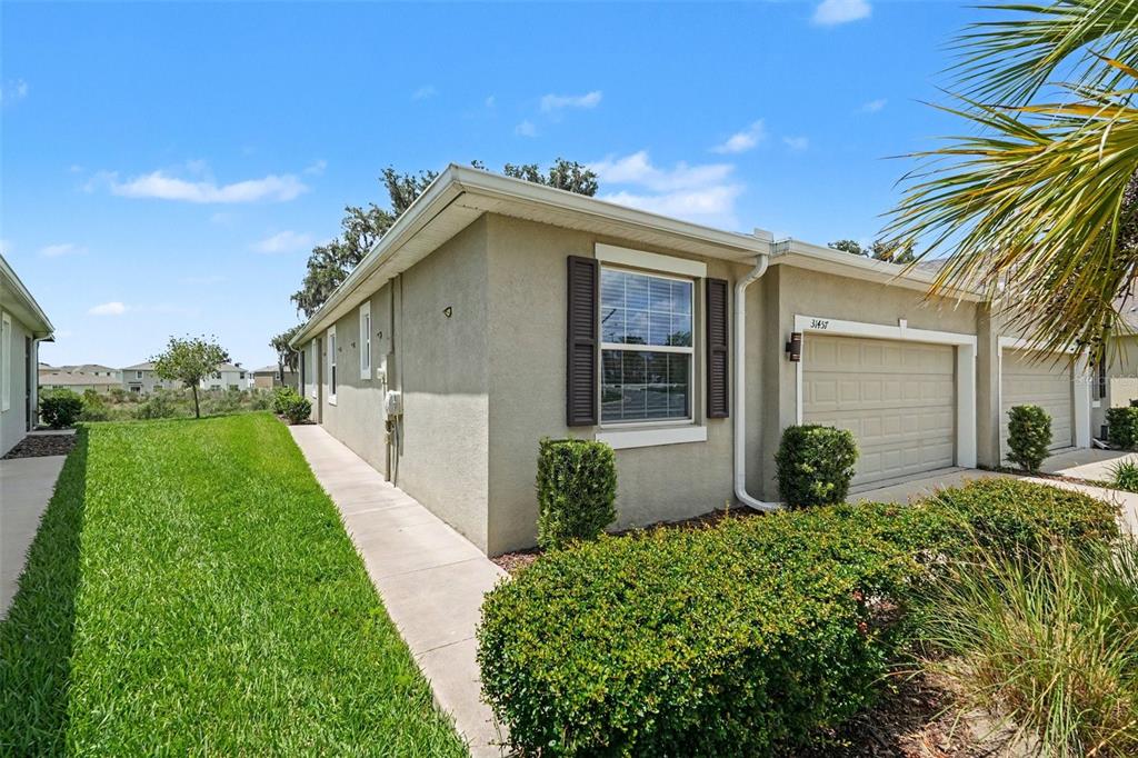 A tan stucco townhouse exterior features a single-car garage, a window with shutters, and landscaping — 31457 MANGO FADE WAY, SAN ANTONIO, FL