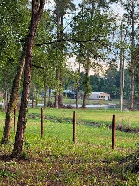 A grassy lot with a fence line leads toward a pond and distant houses — SPRING GARDEN RANCH RD, DE LEON SPRINGS, FL