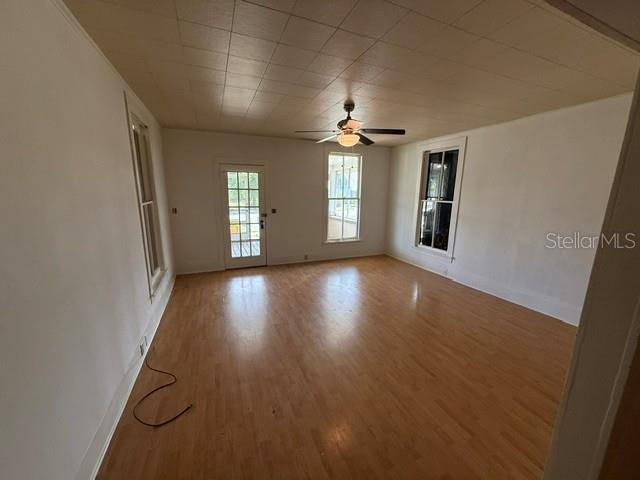 An empty room with light wood flooring, white walls, a ceiling fan, and several windows — 510 E ORANGE AVENUE, EUSTIS, FL
