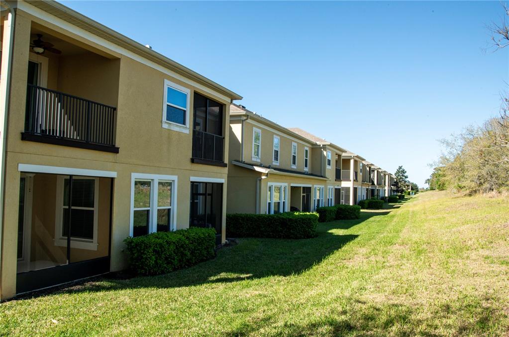 A multi-story apartment building with tan stucco walls, screened balconies, and a grassy lawn — 17459 CHATEAU PINE WAY, CLERMONT, FL