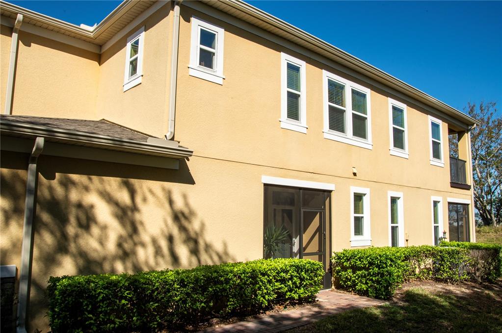 The exterior of a two-story tan stucco building features a screened patio and green hedges — 17459 CHATEAU PINE WAY, CLERMONT, FL