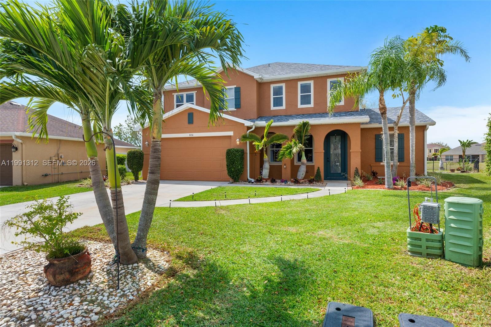 A two-story orange stucco house features a two-car garage and palm trees in the yard — 8130 blue daze ct, Lehigh Acres FL 33972, LEHIGH ACRES, FL