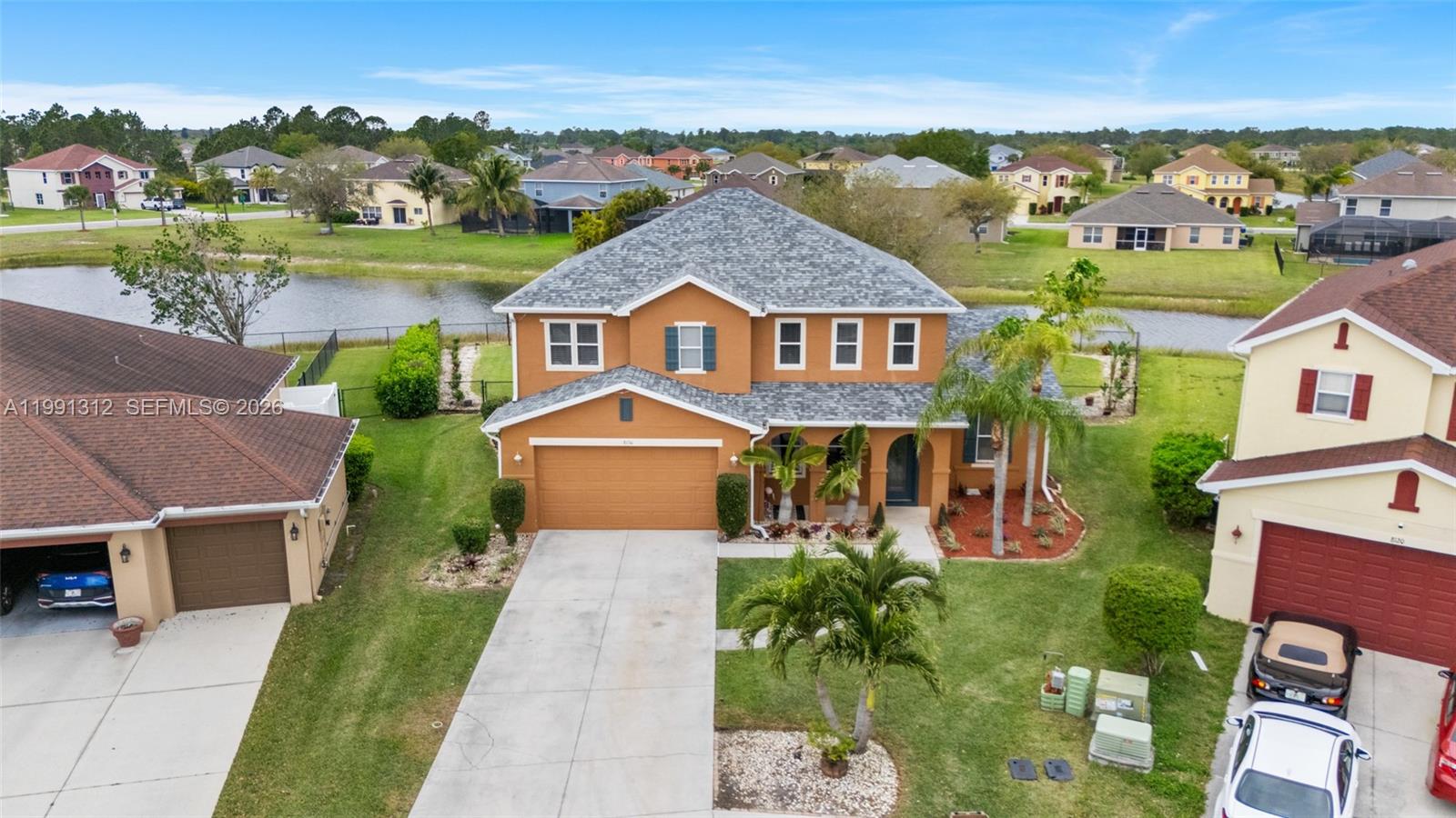 An aerial view shows a two-story orange house with a gray roof and a driveway — 8130 blue daze ct, Lehigh Acres FL 33972, LEHIGH ACRES, FL