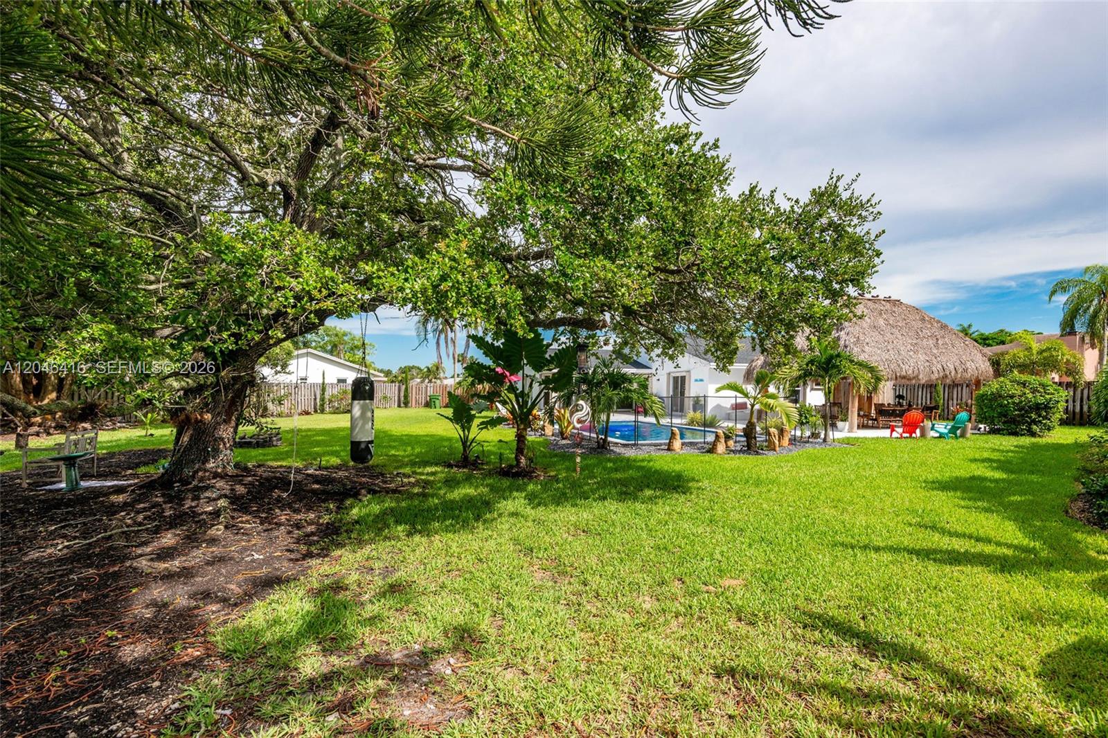 A grassy backyard features a large tree, a punching bag, a swimming pool, and a tiki hut — 16736 SW 5th Way, Weston FL 33326, WESTON, FL