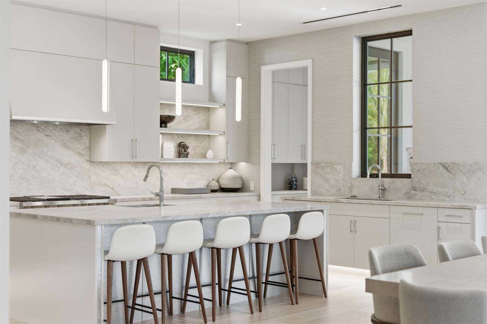A modern kitchen features a marble island with five stools, light cabinetry, and pendant lighting — 210 Cortez Road, West Palm Beach FL 33405, WEST PALM BEACH, FL