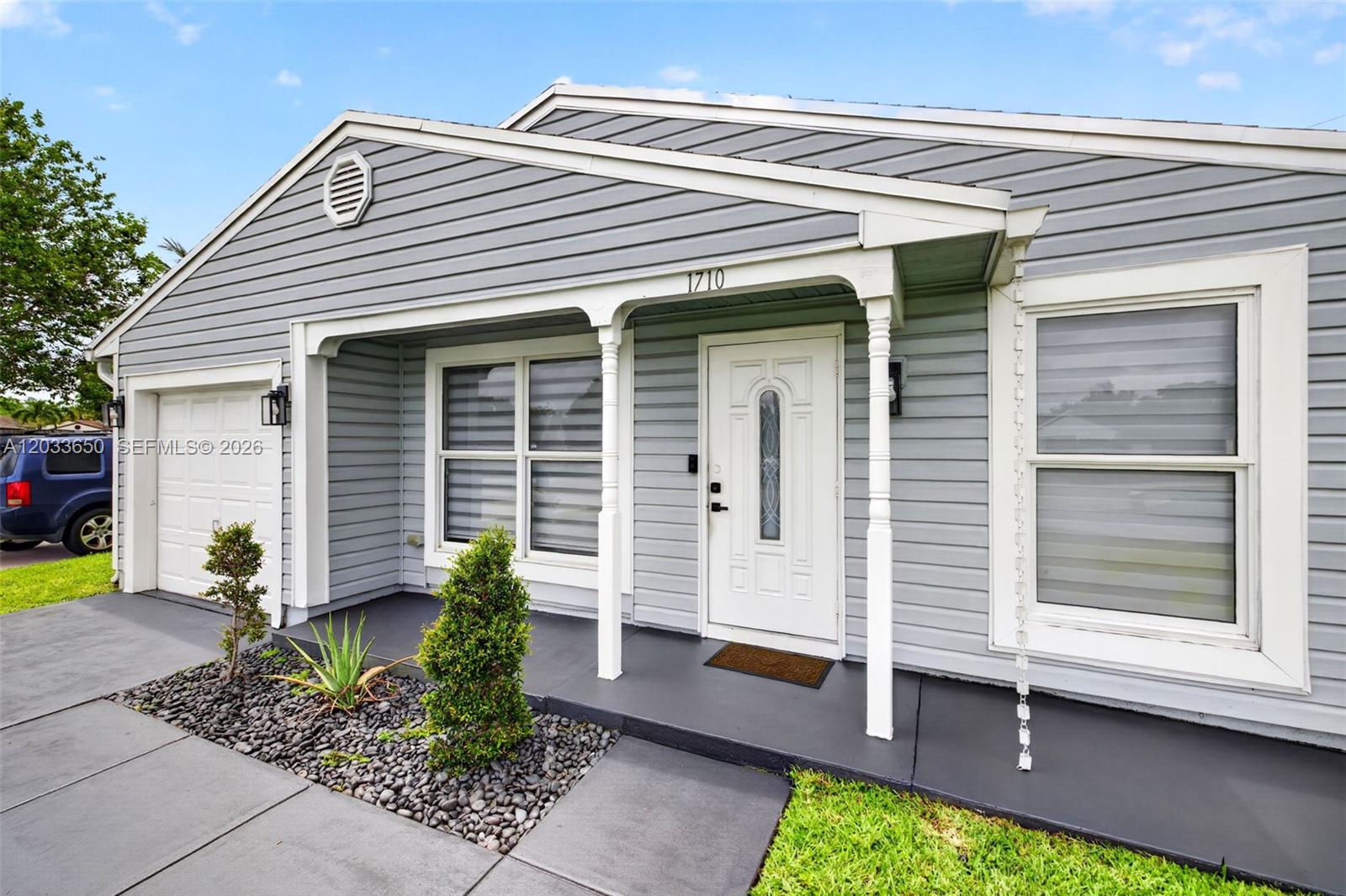 A gray-sided house features a covered front porch, white trim, and a single-car garage — 1710 SW 83rd Ter, Miramar FL 33025, MIRAMAR, FL
