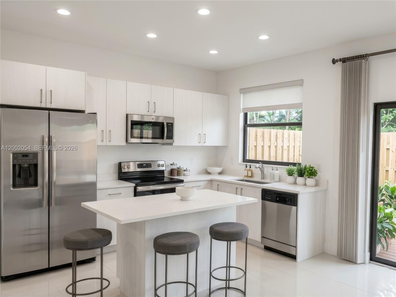 A modern kitchen features white cabinets, stainless steel appliances, a center island, and bar stools — 12525 NW 23rd Pl, Miami FL 33167, MIAMI, FL