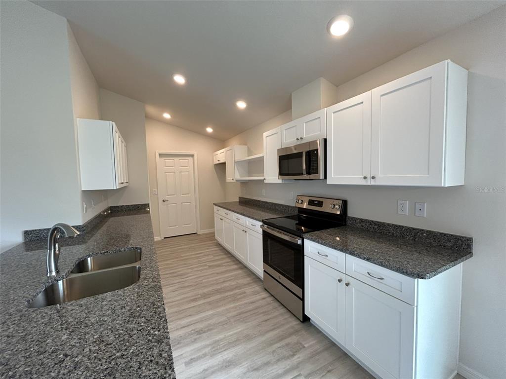 A kitchen features white cabinets, granite countertops, stainless steel appliances, and light wood-look flooring — 8309 N INDIA WAY, CITRUS SPRINGS, FL