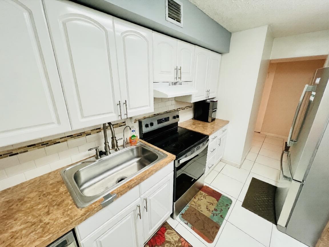 A kitchen features white cabinets, a stainless steel sink, a black stove, and tiled floors — 3821 Environ Boulevard # 203, Lauderhill FL 33319, LAUDERHILL, FL