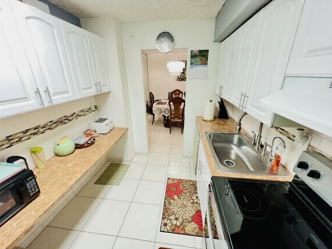 A galley kitchen features white cabinets, a wood-look laminate countertop, and white tile flooring — 3821 Environ Boulevard # 203, Lauderhill FL 33319, LAUDERHILL, FL