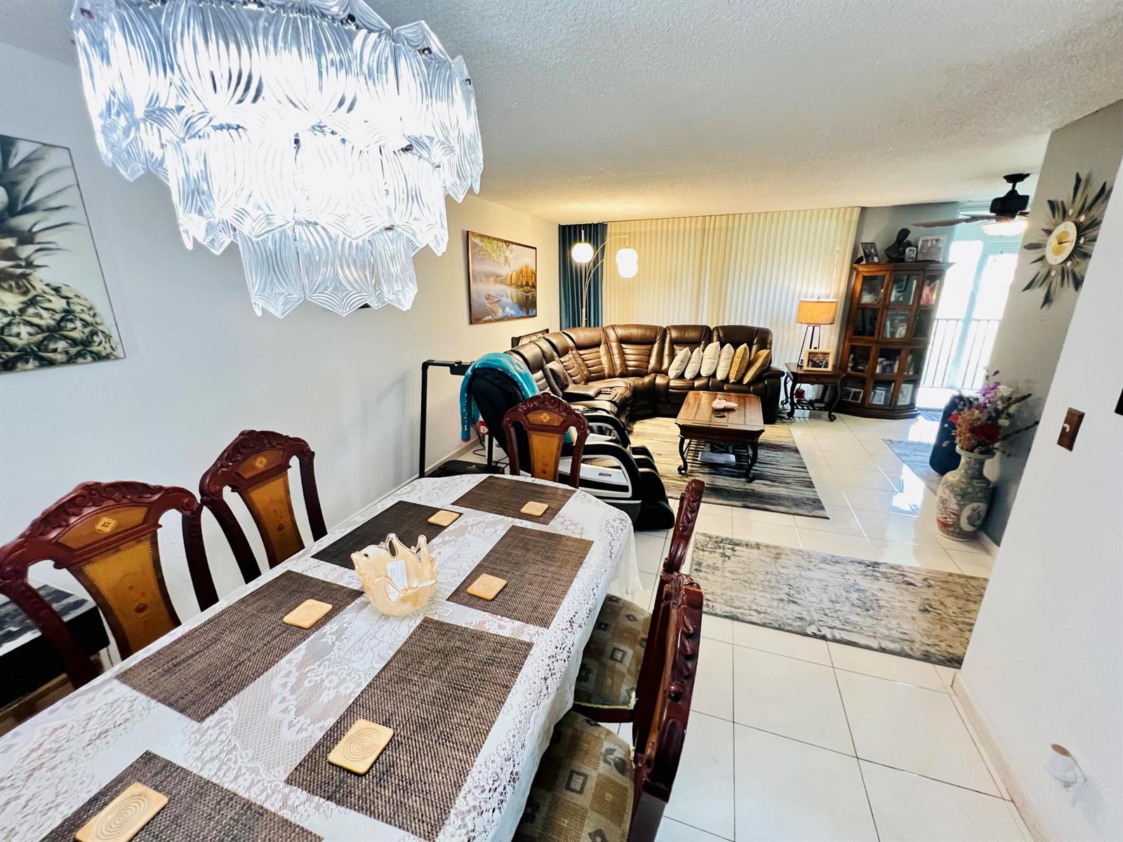 A dining area with a crystal chandelier leads into a living room with leather seating — 3821 Environ Boulevard # 203, Lauderhill FL 33319, LAUDERHILL, FL