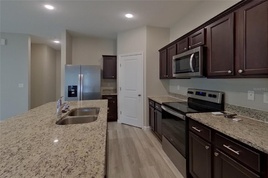 A kitchen features dark wood cabinets, granite countertops, stainless steel appliances, and a central island — 6376 GREEN BUD DRIVE, GROVELAND, FL