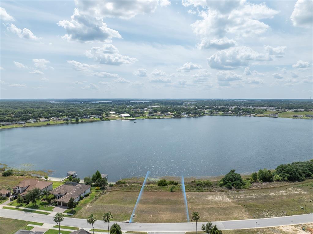 An aerial view shows a vacant waterfront lot with blue boundary lines facing a lake — 4253 JULIANA LAKE DRIVE, AUBURNDALE, FL