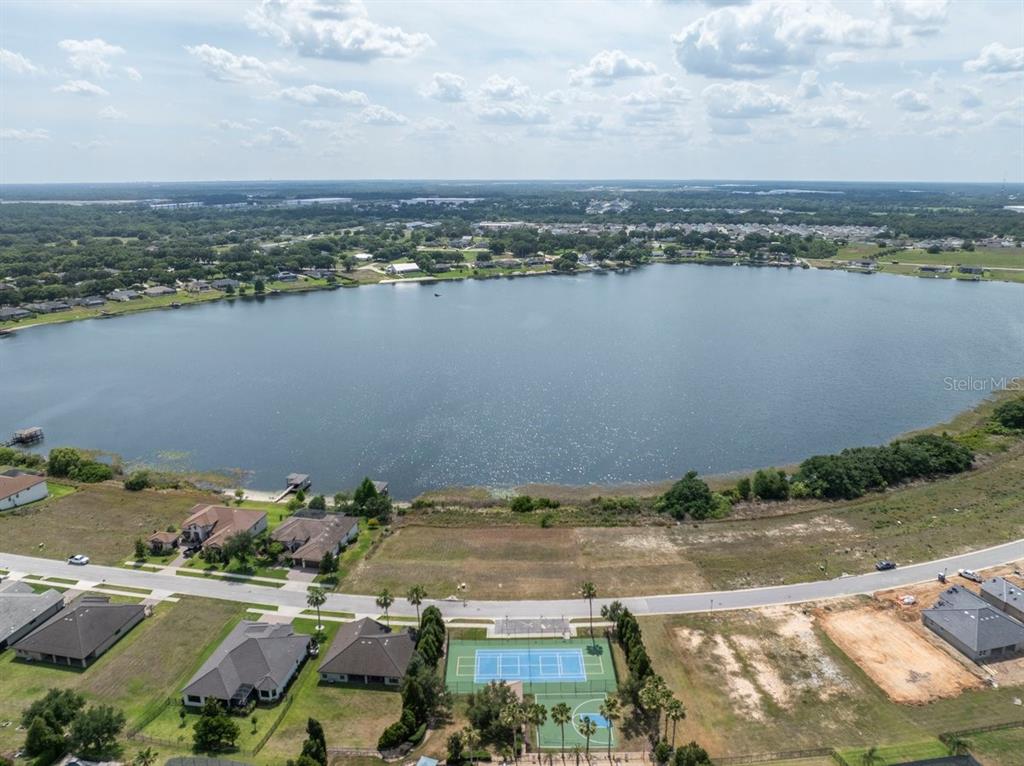 An aerial view shows a lakefront residential neighborhood with a tennis court and vacant lots — 4253 JULIANA LAKE DRIVE, AUBURNDALE, FL