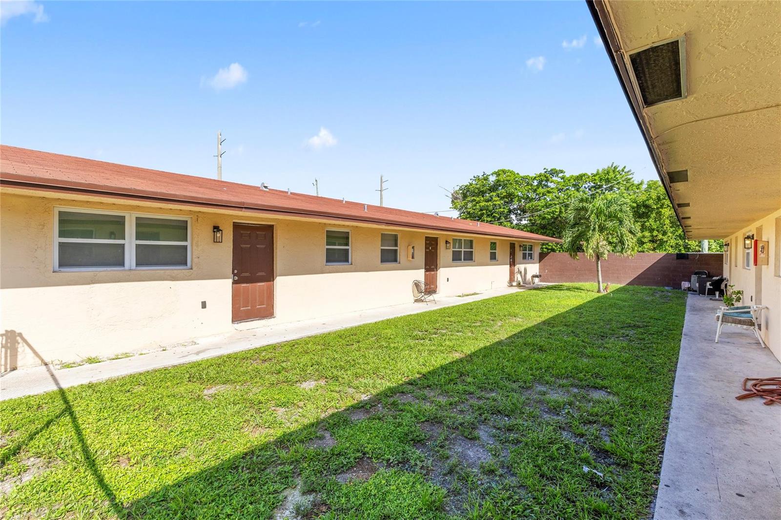 An exterior view of a single-story apartment building with a grassy courtyard and concrete walkway — 237 NW 12th Court, Pompano Beach FL 33060, POMPANO BEACH, FL