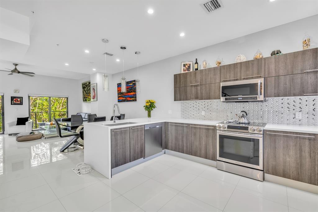 A modern kitchen features dark wood cabinetry, white countertops, stainless steel appliances, and tile flooring — 462 SE 1st Circle, Pompano Beach FL 33060, POMPANO BEACH, FL