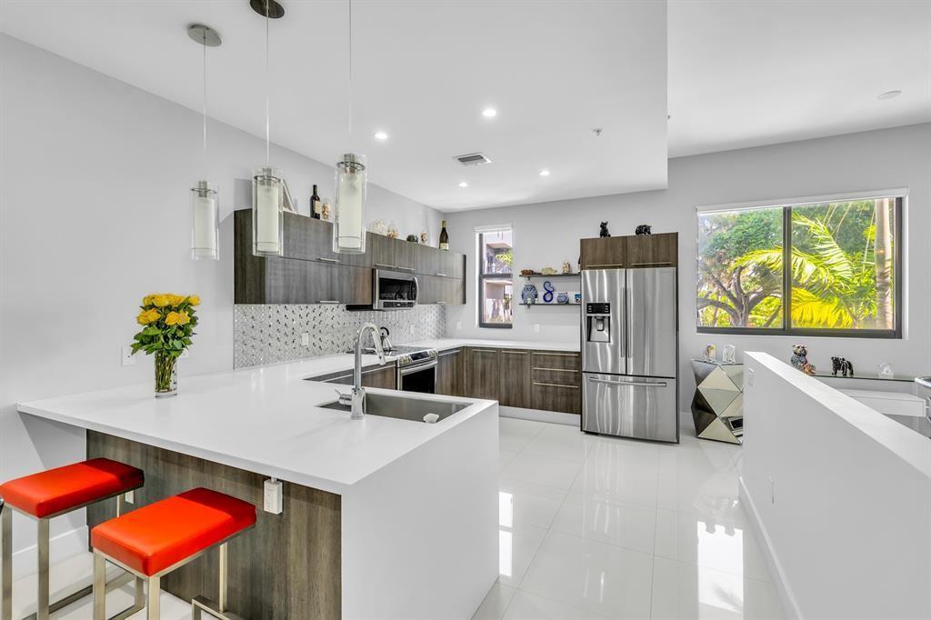 A modern kitchen features white countertops, dark wood cabinetry, stainless steel appliances, and red stools — 462 SE 1st Circle, Pompano Beach FL 33060, POMPANO BEACH, FL