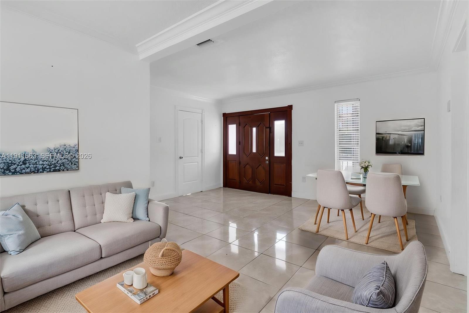 A bright living and dining area features white walls, tile flooring, and a wooden front door — 1101 SW 17 AVE, Miami FL 33135, MIAMI, FL