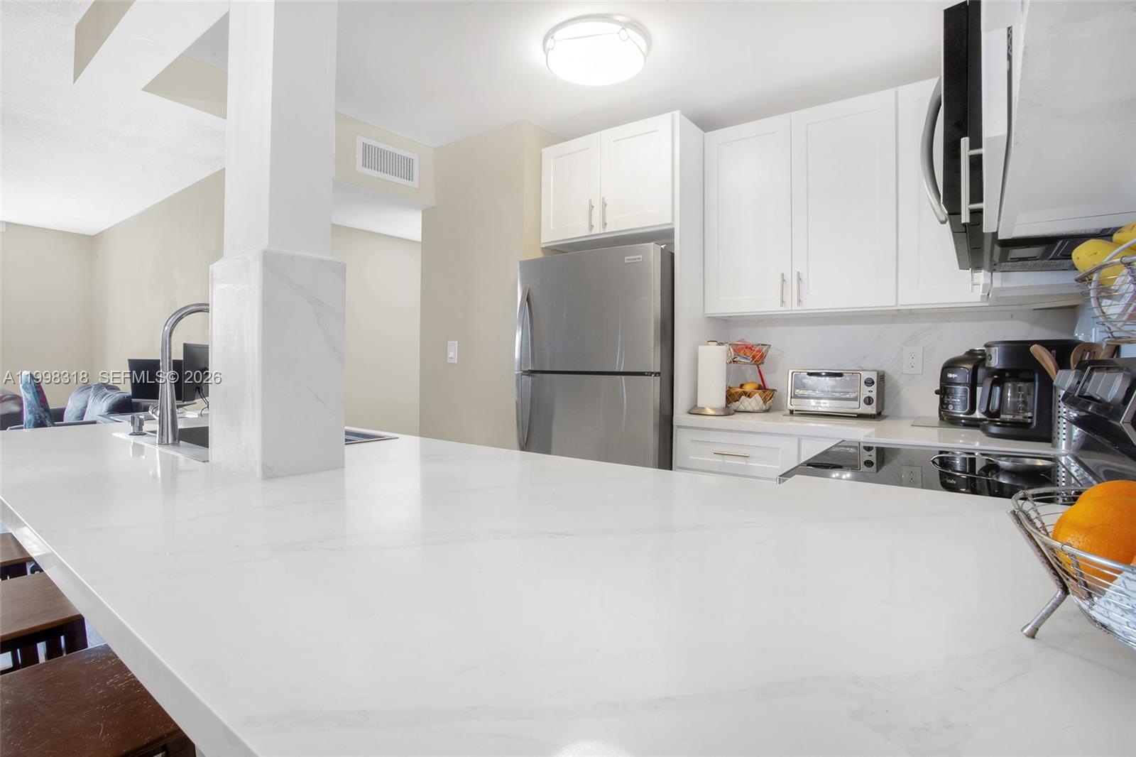 A kitchen features white cabinets, marble-patterned countertops, a breakfast bar with four wooden stools, and stainless steel appliances — 9682 Fontainebleau Blvd # 503, Miami FL 33172, MIAMI, FL