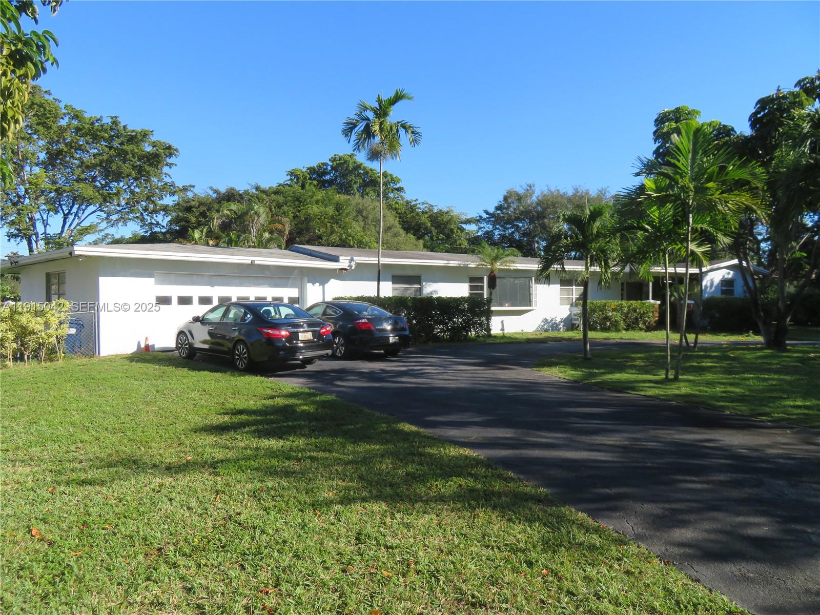 A white single-story house with a driveway and two parked cars sits on a lawn — 7955 SW 131st St, Pinecrest FL 33156, PINECREST, FL