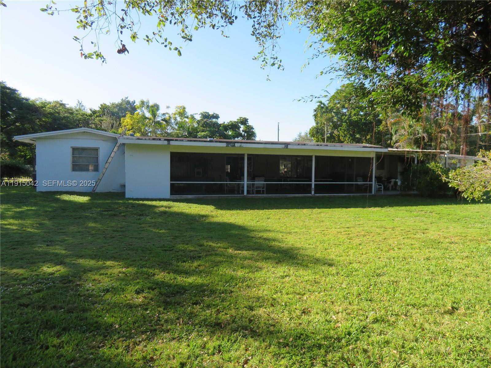 The exterior of a white single-story house features a large screened-in patio and backyard — 7955 SW 131st St, Pinecrest FL 33156, PINECREST, FL