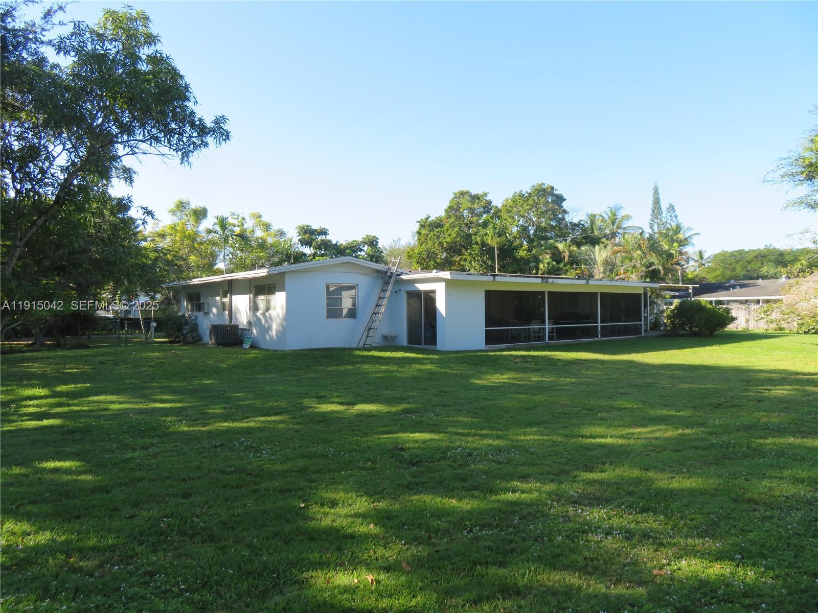 The rear exterior of a white single-story house features a large screened-in porch and lawn — 7955 SW 131st St, Pinecrest FL 33156, PINECREST, FL
