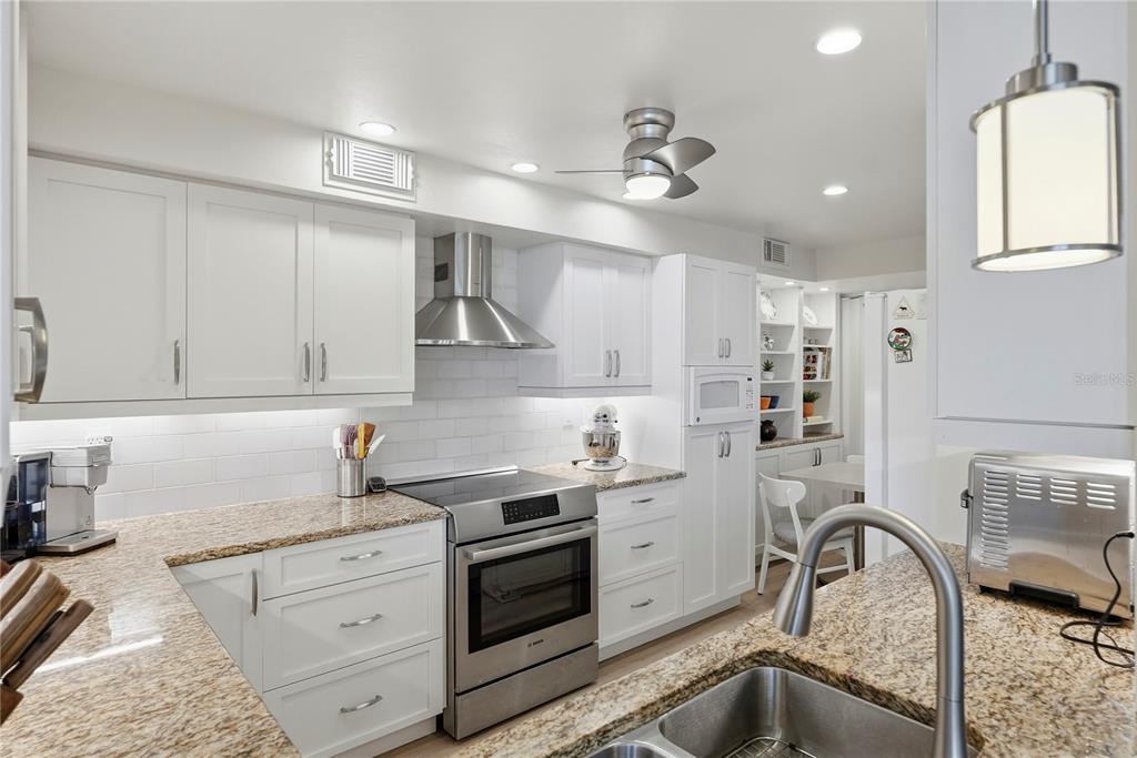 A bright kitchen features white cabinets, granite countertops, stainless steel appliances, and a subway tile backsplash — 5729 PUERTA DEL SOL BOULEVARD S UNIT 181, ST PETERSBURG, FL