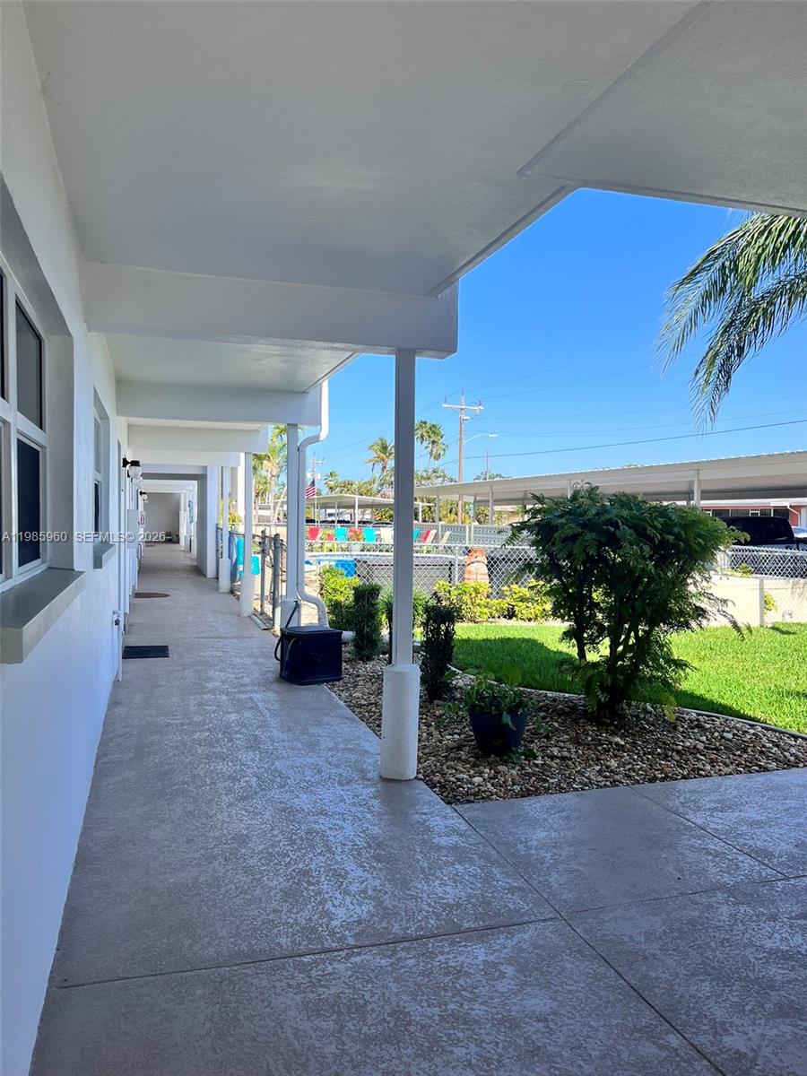 A covered outdoor walkway leads past a building exterior toward a fenced pool area — 708 Victoria Dr # 101, Cape Coral FL 33904, CAPE CORAL, FL